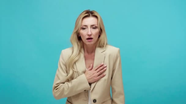 胸に息をしようとすると 心臓の問題 心臓発作 緊急事態のリスクを胸の痛みを感じるビジネススーツの中年齢女性の動揺を抑制 青い背景に隔離された屋内スタジオショット — ストック動画