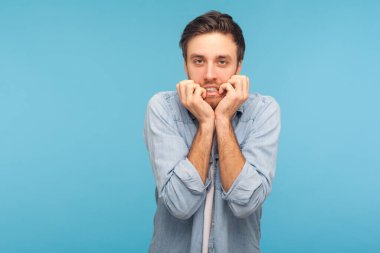 Anksiyete bozukluğu, depresyon. Stresli, endişeli, işçi kot gömleği giyen, çivi yiyen, beladan korkan, panikleyen ve korkmuş görünen bir adamın portresi. Stüdyo çekimi mavi arkaplanda izole edildi 