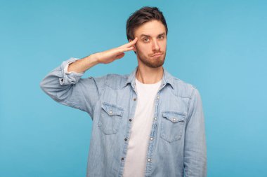 Evet, efendim! İşçi kot gömleği giyen sorumlu vatansever bir adamın portresi. Komutandan emir bekleyen, disipline itaat eden bir asker gibi saygıyla selamlanıyor. Stüdyo çekimi mavi arkaplanda izole edildi 