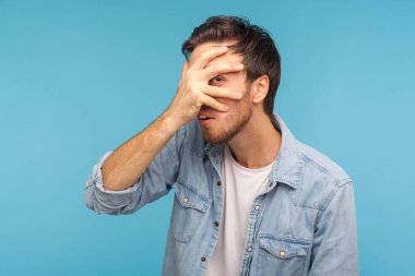 Vay canına, nedir bu? Meraklı işçi kot gömleği giymiş meraklı bir adamın portresi. Şaşırmış ve meraklı bir ifadeyle parmaklarının arasından bakıyor. Yasak içeriği izliyor, gizli casusluk yapıyor. Stüdyo çekimi izole 