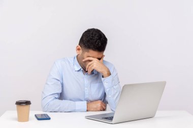 Ofiste çalışan üzgün bir adam dizüstü bilgisayarla oturuyor, başını eğip ağlıyor, depresif hissediyor, iş sorunları için endişeleniyor, işini kaybediyor. Beyaz arka planda izole edilmiş kapalı stüdyo çekimi 