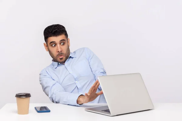 Scared frightened man employee sitting office workplace, showing stop to laptop screen with video call, looking terrified, afraid to watch horror content. studio shot isolated on white background