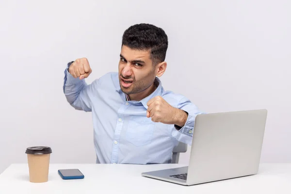 Mad man boss sitting office workplace with laptop, punching to camera and looking furious, boxing threatening to hit, anger management, aggression at work. studio shot isolated on white background