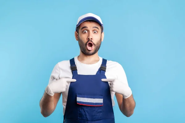 Wow this is me! Surprised handyman in overalls pointing himself, shocked and proud of achievement. Profession of service industry, courier delivery, housekeeping maintenance. studio shot isolated