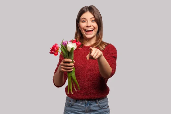 给你的花 一个快乐快乐的黑发女孩的画像 微笑着 捧着郁金香花束 指着相机 在春节假期祝贺你 在灰色背景下隔离的室内拍摄 — 图库照片