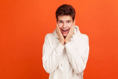 Vay canına! Piyangodaki zaferi karşısında şaşkına dönmüş, ağzı açık ve kocaman gözleriyle kameraya bakan sıradan bir genç adam. Turuncu arka planda kapalı stüdyo çekimleri
