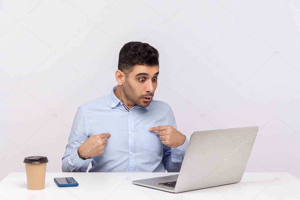 Really, me? Amazed businessman sitting office workplace, pointing himself and looking at laptop screen with shocked expression, talking on video call. indoor studio shot isolated on white background
