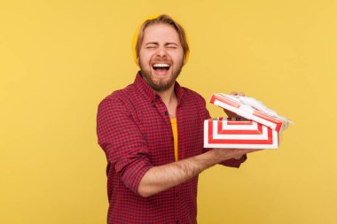 Şapka hediye kutusundaki neşeli, neşeli hippi çocuk. İçten ve şaşırmış bir şekilde gülüyor. Muhteşem doğum günü hediyesi karşısında heyecanlanıyor. Stüdyo çekimi sarı arkaplanda izole edildi