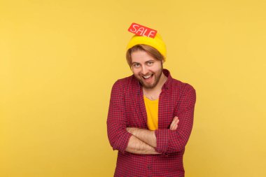 Neşeli modacı hippi şapkasıyla ayakta duruyor, kameraya bakıyor dişlek gülüşüyle, indirimli sevinçle, Kara Cuma indirimleriyle. Sarı arka planda izole edilmiş kapalı stüdyo çekimi