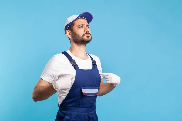 This is me! Egoistic handyman in overalls pointing himself and looking with arrogance, proud of achievement. Profession of service industry, courier delivery, housekeeping maintenance. studio shot