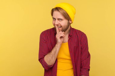 Shh, sessiz ol! Şapkalı ve damalı gömlekli komik hippi sakallı adam. Dudaklarında parmak, el hareketleriyle şşş yapıyor. Gülümsüyor, gizemli bir şekilde gizlilik istiyor. Stüdyoda çekim izole edildi