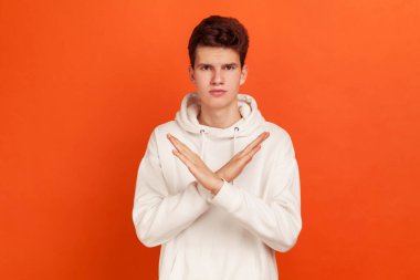 İmkanı yok! Şık kapüşonlu, kollarını kavuşturmadan kötü alışkanlıklara ve bağımlılığa hayır diyen ciddi odaklanmış genç bir adam. Turuncu arka planda kapalı stüdyo çekimleri