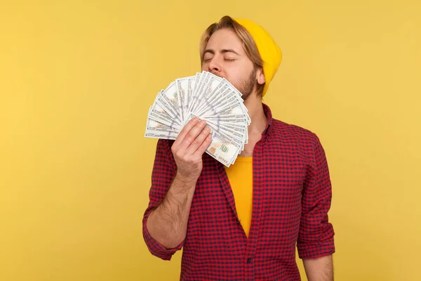 豊かな悪意のあるヒップスター男ビーニー帽子と小切手シャツの喜びの表現でドル紙幣の匂い 貪欲なお金に取りつかれ 大きな宝くじの勝利 黄色の背景に隔離されたスタジオショット — ストック写真