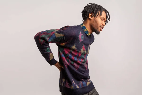 Profile portrait african man with dreadlock cant straighten, suffering from cramped back, health problems, renal colic. Indoor studio shot isolated on gray background