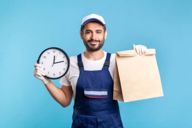Yemek teslimatı, zamanında nakliye! Tamirci portresi, saat tutan eldivenler ve paket. Kurye taşımacılığı, posta hizmetleri. Mavi arka planda kapalı stüdyo çekimleri