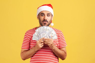 Noel Baba şapkalı, sakallı, elinde dolarlarla yılbaşı hediyesi almaya hazır, ödünç vermeye hazır heyecanlı bir adam. Sarı arka planda kapalı stüdyo çekimleri