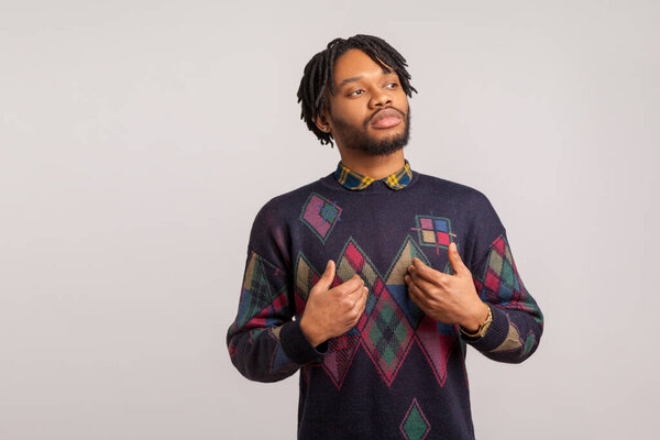 Self confident egoistic guy with dreadlocks pointing hands on himself with arrogant face, proud of start up. Indoor studio shot isolated on gray background