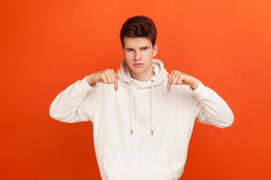 Patronluk taslayan, şık kapüşonlu, şık bir genç adam. Parmakla işaret ediyor, burayı ve şu anı talep ediyor. Turuncu arka planda kapalı stüdyo çekimleri
