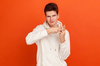 Kapüşonlu kapüşonlu, kapüşonlu popüler erkek blog yazarı parmaklarıyla etiket işareti gösteriyor ve popüler web sitelerini tavsiye ediyor. Turuncu arka planda kapalı stüdyo çekimleri