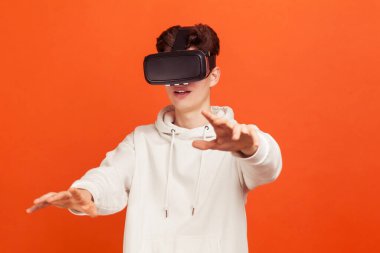 Gelişigüzel giyinmiş kapüşonlu genç sanal gerçeklik kulaklığı takan, gelecekten gelen 3 boyutlu vizyon kullanan yeni teknolojiler keşfediyor. Turuncu arka planda kapalı stüdyo çekimleri