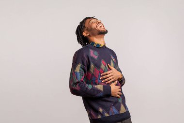 Yandan bakıldığında son derece heyecanlı ve mutlu bir Afrikalı adam. Rasta saçlarıyla gülüyor, elleriyle karnını tutuyor, komik bir şaka, anekdot. Gri arka planda izole edilmiş kapalı stüdyo görüntüleri