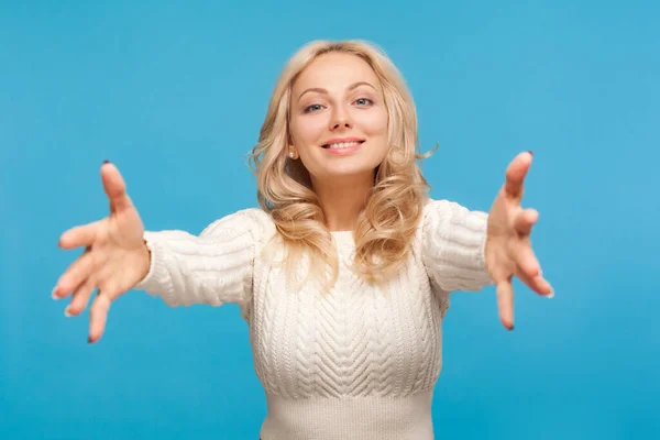 Come here and hug me. Happy attractive woman with curly blond hair spreading arms ready to embracing, excitement. Indoor studio shot isolated on blue background