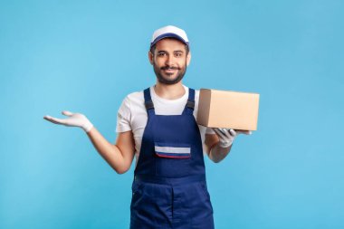 Üniformalı mutlu işçi karton kutu taşıyor ve diğer elini boş alanı tutmak için kaldırıyor. Ticari imaj için reklam alanı. Kargo taşımacılığı, teslimat hizmeti, ekspres nakliye