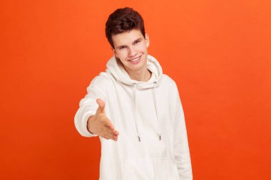 Hoş bir gülümsemesi olan samimi bir genç adam el sıkışmak için elini uzatıyor, tanıştığımıza memnun oldum, tanıdık. Turuncu arka planda kapalı stüdyo çekimleri