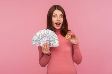 El ele tutuşan esmer kadın hayrete düştü dolar ve bitcoin, kripto para, para ve zenginlik değişimi. Pembe arka planda kapalı stüdyo çekimleri