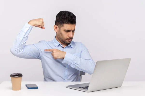 Strong confident man boss sitting office workplace, showing biceps to laptop screen when talking on video call, feeling power, boasting success in business. studio shot isolated on white background