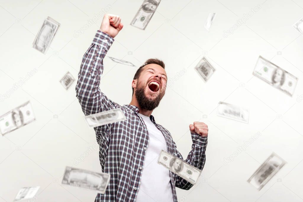 Hurray I am winner and rich now! Portrait of winner man raising hands, screaming yes i did it, joyful reacting to success, victory. money rain falling from up. indoor, isolated on white background