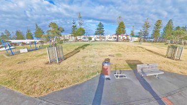 Çimenli bir tarla ile alçak binalar arasında uzanan güneşli bir sahil yolu.. 