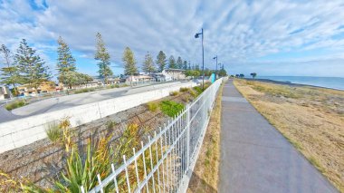 Beton rampaları ve tribünleri olan bir kaykay parkı bulutlu bir gökyüzünün altında beyaz bir çitin arkasında görülüyor.