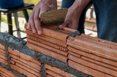 Duvarcı işçisi dış duvara tuğla döşüyordu..