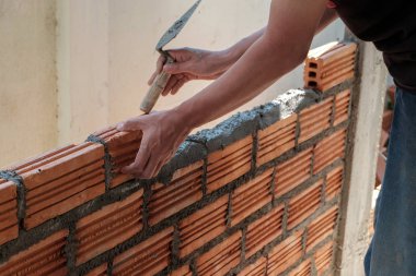 Duvarcı işçisi dış duvara tuğla döşüyordu..