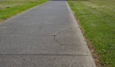 Üstünde belgili tanımlık yan yol yeşil çim ile yürüyüş üzerinde kırık asfalt