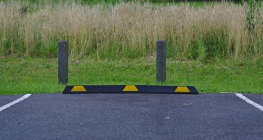 Rubber parking block in black and yellow colors on asphalt surface with wild grass background clipart