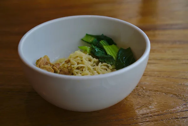 Chicken noodle with green veggie in white bowl on wooden table