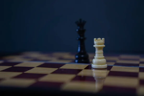 White rook and black king chess pieces softly blurred in background on chessboard