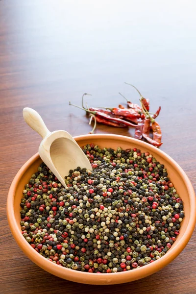 colored peppercorns in a ceramic bowl with hot chillies on background