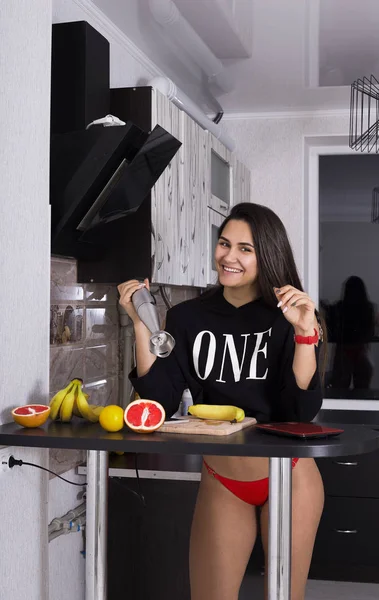 young sports girl in the underwear in the kitchen prepares sports food from fruit. using a blender