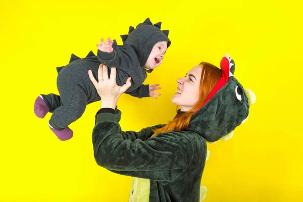 mom and daughter in a funny dragon costume. play on a yellow bac