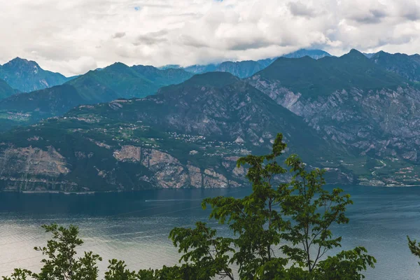 Gray Cumulonimbus clouds over the mountain range and lake. Italian Alps near lake Garda.