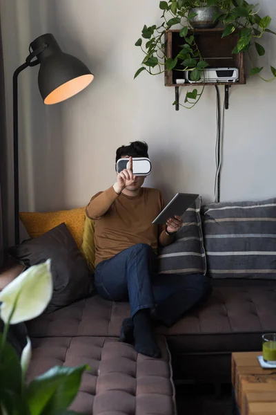 自宅のリビング ルームでデジタル タブレットを使用して仮想現実ヘッドセットの男 — ストック写真