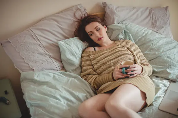 Kahve Fincanı Tutarak Evde Yatakta Yatarken Düşünceli Kadın — Stok fotoğraf