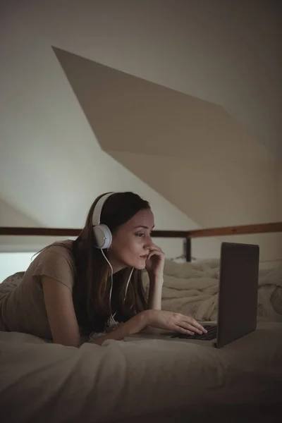 在家中使用笔记本电脑的带耳机的妇女 — 图库照片