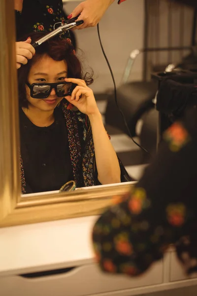 时尚的女人在专业的发廊做头发的时候 翻看太阳镜 — 图库照片