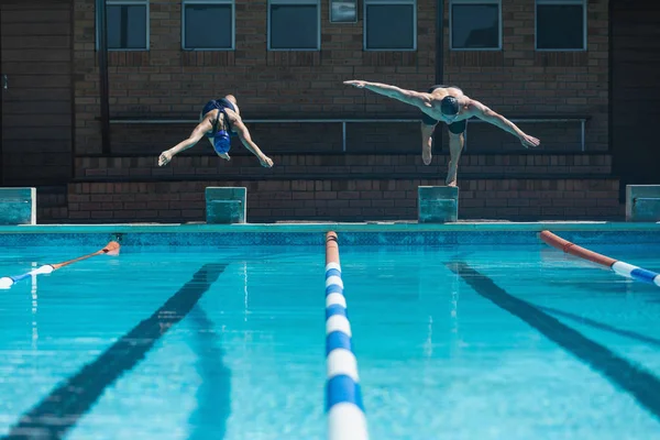 日差しの中でのスイミング プールで同時に水に飛び込む男性と女性の白人選手の正面図 — ストック写真