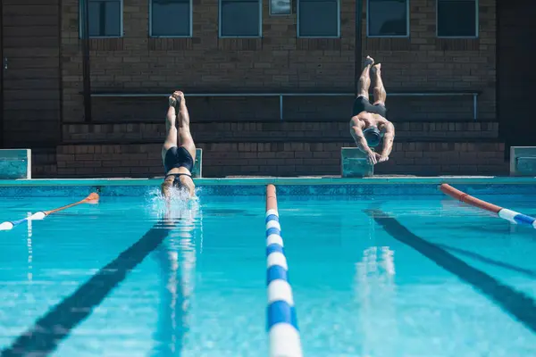 日差しの中でのスイミング プールで同時に水に飛び込む男性と女性の白人選手の正面図 — ストック写真