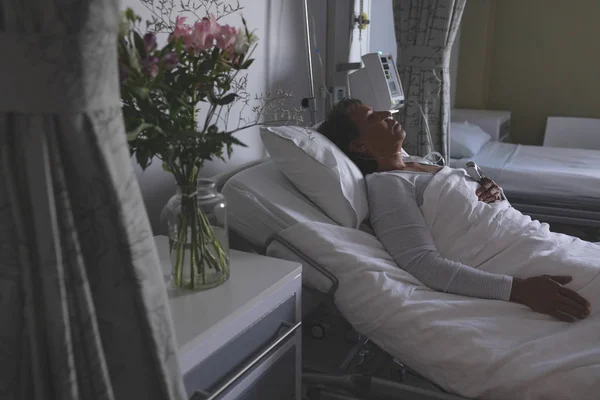 病院の病棟でベッドで寝ている美しい混合人種女性患者の高角図 花はベッドの隣の食器棚の花瓶の中に立っている — ストック写真